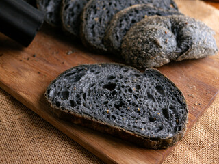 Fresh baked black charcoal sourdough ciabatta bread sliced on wooden board.