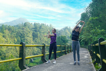 Asian Women Stretching Outdoors on a Forest Bridge for Exercise and Wellness