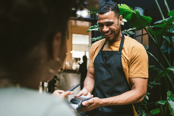 Happy waiter accepting contactless payment from customer in cafe