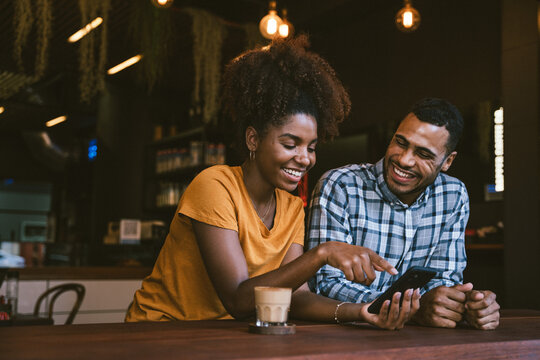 Happy young couple using smartphone and enjoying coffee while sitting in cafe