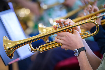Obraz premium A trumpet being played by a youth in the foreground with other trumpets blurred in the background.