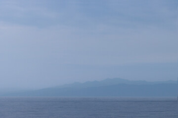 Landscape background of silhouette mountain range and blue sea with hazy sky, copy space