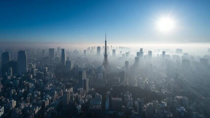 High angle view of a cityscape shrouded in morning mist, with a tall tower silhouetted against a bright sun and clear blue sky. Buildings are dark against the light, creating a moody atmosphere. - Powered by Adobe