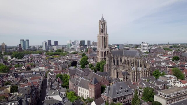 Closeup of De Dom church tower in Utrecht within medieval town and high rise modern buildings on horizon behinc. Holland religious tourist destination seen from above.