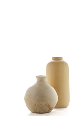 Vertical image of two modern minimalist vases in soft sand tones, backlit with bright white light. The elegant simplicity and neutral palette