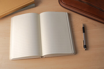 Top-down view of an open blank lined notebook on a light wooden desk, with a black and silver pen, a leather case, and journal. perfect for themes of journaling, planning, education, or office work.