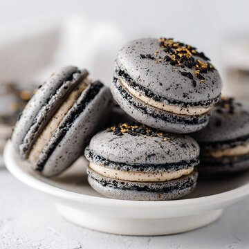 Close up of a stack of gray macarons with black and gold sprinkles on a white plate surface view