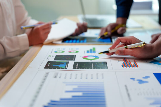 Business team analyzing financial data using printed graphs and charts, pens and a digital tablet, working together on a wooden table