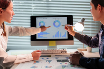 Business colleagues reviewing financial data displayed on a computer screen, pointing at charts and graphs during a collaborative working session
