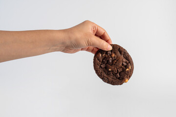A large chocolate cookie topped with chocolate chips and hand, set against a white background.