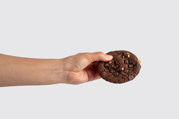 A large chocolate cookie topped with chocolate chips and hand, set against a white background.