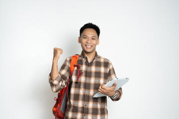 A cheerful young man in a plaid shirt, holding a tablet and backpack confidently, expressing enthusiasm and success. Perfect for themes of education, technology, achievement, and youthful energy.