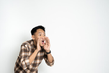 Asian young man wearing a checkered shirt expressing excitement, shouting enthusiastically, on a plain background. Ideal for concepts like communication, announcement, joy, and energy.