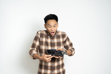 Surprised Asian Man Looking at an Empty Wallet on a White Background. Depicting financial concerns or unexpected expenses.
