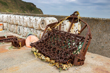 Old rusty scallop dragging and lobster pots trapscommercial fishing equipment at a fishing harbour dock.