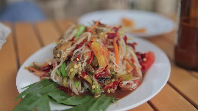 Authentic Thai spicy rice noodle papaya salad (Som Tum Sen Khao Poon) served on a dining table. Vibrant colors and delicious Asian cuisine.