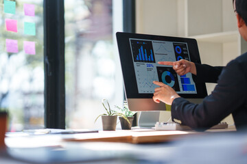 Business colleagues pointing at computer screen showing financial data, analyzing charts and graphs, discussing market trends and investment strategies in modern office