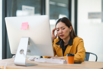 Young Asian businesswoman suffering from headache, migraine or stress while working on computer at her desk