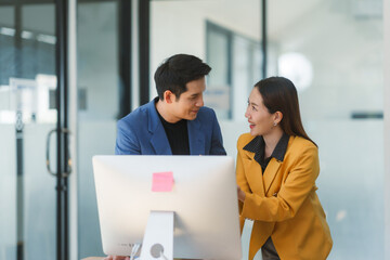 Two asian business partners discussing work while looking at desktop computer in modern office