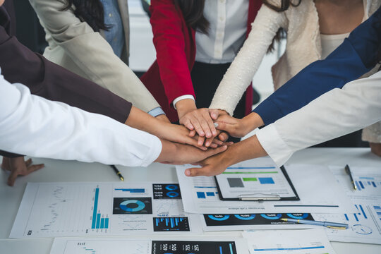 Business people joining hands over a table with financial charts, showing teamwork and collaboration