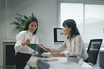 Two smiling businesswomen analyzing financial data with graphs on a clipboard during a meeting in the office