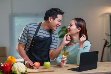 Young asian couple having fun cooking together in the kitchen, preparing healthy food and drinking wine