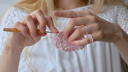 Caucasian girl crocheting a delicate pink lace product. 