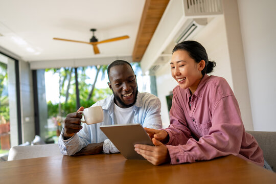 Happy young diverse, multiethnic couple planning budget, reading good news on digital tablet at home