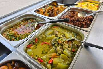 A colorful selection of Thai street food curries and stir-fried dishes served in stainless steel trays at a local mixed rice vendor.