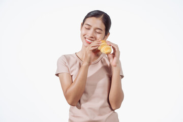 A confident young Asian woman in a light brown shirt stands against a white background, happily holding a delicious croissant in her hand, ready to enjoy a fresh and tasty pastry snack.
