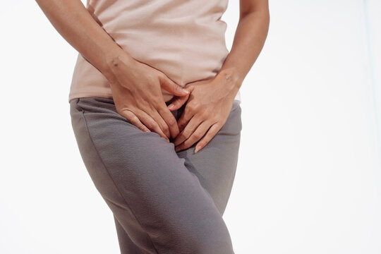 Confident young Asian woman in light brown shirt stands against a white background, experiencing vaginal pain. inflammation, cysts, endometriosis gynecological conditions affecting female health.