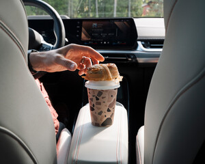 man reaching for a bun sitting on a take away coffee in the car