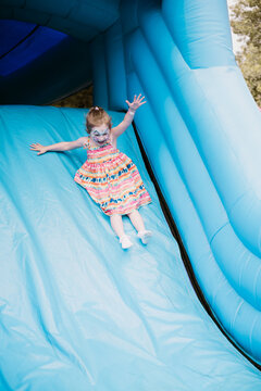 Toddler girl sliding on a bouncy castle, summer holiday