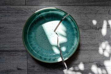 Cracked turquoise ceramic plate in sunlight lying on a wooden surface.