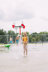 Smiling child standing in sprinklers while kids play in splash pad