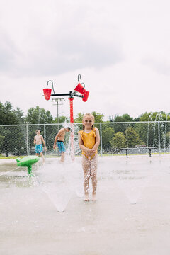 Smiling child standing in sprinklers while kids play in splash pad