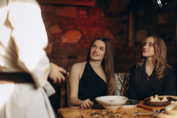 Two Women Enjoying Dinner While Interacting with a Waiter in a Restaurant