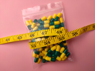 Closeup of a medicine pill package with measuring tape on a pink background