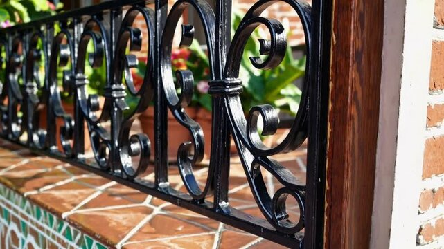 Ornate black metal railing with decorative scrollwork charming brick balcony, vibrant terracotta tiles, potted plants