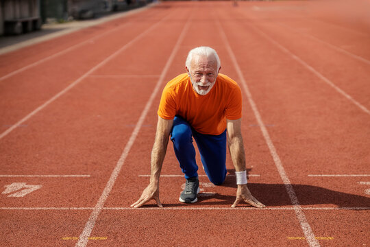 Front view of senior sportsman on starting line on stadium preparing for sprinting.