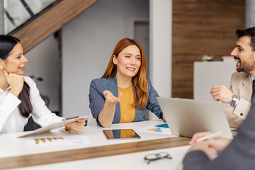 Portrait of smiling businesswoman sitting at conference table in gender balanced collective and discussing project.
