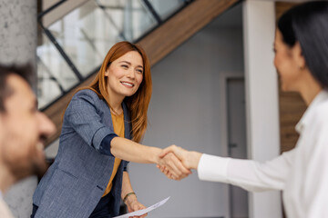 Naklejka na ściany i meble Two female leaders shaking hands during the meeting at minimalistic office.