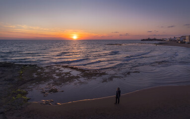 Woman Gazes at the Vibrant Sunset Over the Tranquil Sea in Punta Secca, Sicily, Italy