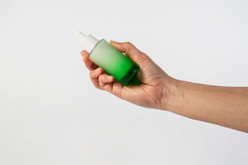 Green glass cosmetic bottle, Skin care or sunscreen cosmetic with hand on white background.