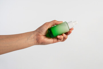 Green glass cosmetic bottle, Skin care or sunscreen cosmetic with hand on white background.
