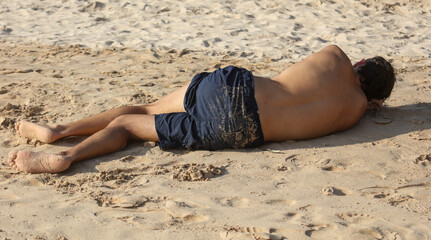 A man is laying on the beach in a blue swimsuit