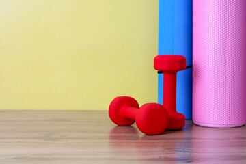 a sports background with dumbbells, a foam fitness roller and a blue yoga mat near a yellow wall....