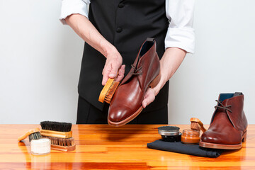 Footwear Ideas. Hands of Professional Male Shoes Cleaner with Cleaning Brushes For Tan Derby...