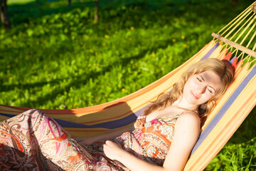 Relaxed Resting Young Winsome Caucasian Blond Sexy Female Posing in Hammock Outdoors Over Green Field Background