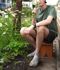 young gardener holding a bouquet of white daisies sitting near a flower bed